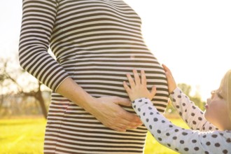 Young child touching the pregnant belly of her mother in beautiful evening sunlight