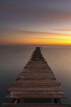 Peaceful sunrise seascape with an old wooden dock leading out into the calm ocean waters