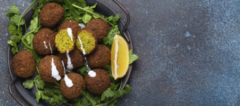 Plate of fried falafel balls served with fresh green cilantro and lemon top view on rustic concrete