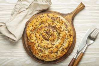 Burek made of filo dough with filling on cutting board, white wooden rustic background top view.