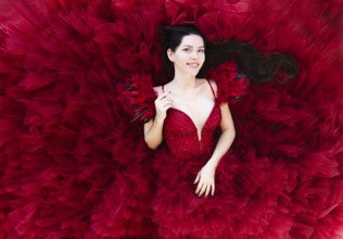 From above of lying beautiful young brunette female in luxurious red evening gown looking at camera