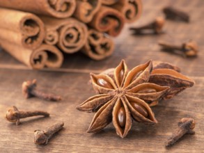 Star anise on wooden background close up. Blurred clove and cinnamon sticks as background