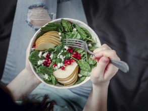 Woman in jeans holding vegan salad bowl with spinach, pear, pomegranate, cheese. Vegan breakfast,