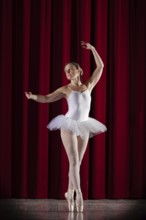 Ballet dancer in white ballet tutu in front of a red stage curtain in elegant pose, Mindelheim City