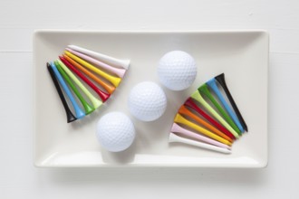 White ceramic dishes with golf balls and wooden tees on over white background, rectangle dish