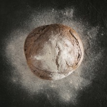 Whole homemade rye bread with rye flour on black textured background. Top view or flat-lay. Low key