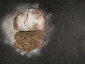 Sliced homemade sourdough rye bread with rye flour on black textured background. Top view or