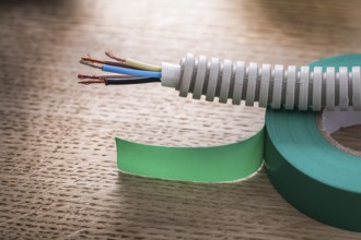 Electric cable in corrugated pipe on roll of green insulating tape