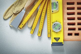Red brick protective gloves putty knife construction level wooden meter on concrete background
