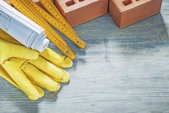 Composition of red bricks protective gloves blueprints wooden meter on wood board construction