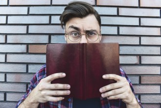 Funny face. Young hipster guy wearing eyeglasses with picked up one browe looking at camera and