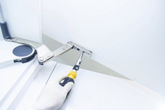 Close-up of a gloved hand fixing a cabinet hinge with a screwdriver