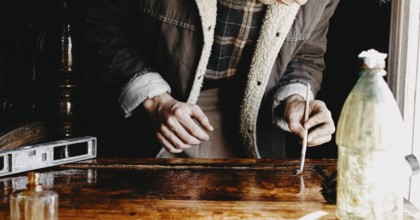 A person concentrated on applying varnish on wood with a bottle nearby