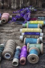 Spools of thread on the old wooden background decorated with branches blossoming lavender.selective