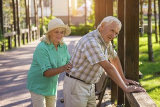 Senior male leans on fence. Elderly couple outdoors. Pains in lower back. Old traumas influence