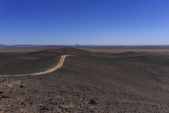 A view of a dirt road leading through the rock and sand desert of southeastern Morocco mear