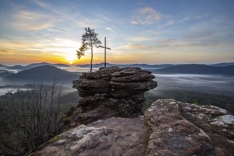 Landscape shot of nature in the morning. Mist in the valley and a summit cross on a sandstone cliff
