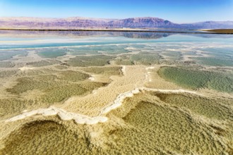 Dead Sea. The green water of the salty sea is surrounded by pink mountains. Evaporated salt forms
