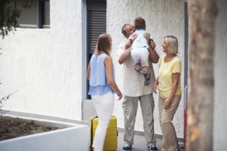 Grandfather greeting his young grandchild lifting him in the air and kissing him as he arrives on a