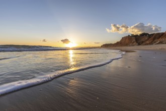 Beautiful sandy beach with red rocks and cliffs. Twilight at sunset with shallow waves on the