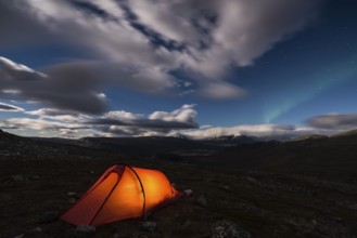 Northern Lights (Aurora borealis) over illuminated tent, Rapadalen, Sarek National Park, Laponia