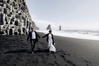 Destination Iceland wedding. A wedding couple walks along the sandy black beach of Vik, near the
