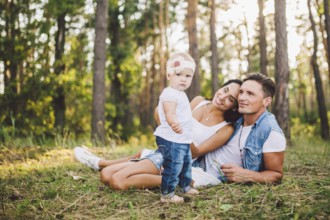 Little girl one year on the background of parents resting on graß learning to walk on nature in the