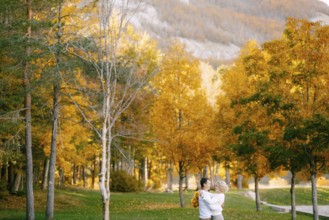 Portrait of smiling man hugging woman with wreath of yellow leaves in autumn forest.