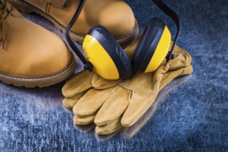 Leather safety boots gloves and noise insulation ear muffs on scratched metallic background