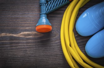 Twisted rubber hose with spray nozzle and gumboots on vintage wooden board gardening concept