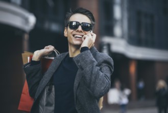 Positive cool guy with sunglasses and paper bags walking near showcase with reflection