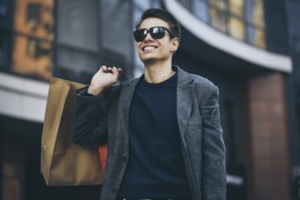 Serious cool guy with sunglasses and paper bags walking at street