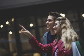 Beautiful couple with shopping bags is talking and smiling while doing shopping in the mall focus