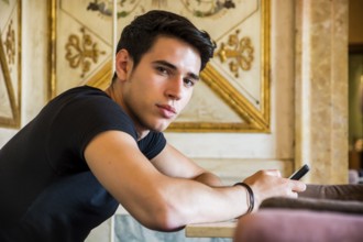 Young handsome man sitting in elegant cafeteria or restaurant using cell phone to send text message