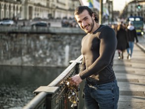 Side view of bearded man in casual clothes standing on footbridge and attaching love lock to metal