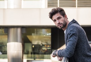 One attractive man in urban environment in city, leaning on handrail, wearing cardigan