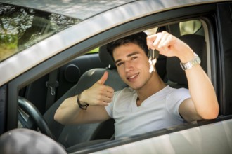 Young handsome male sitting in car and showing big thumb and keys while smiling at camera