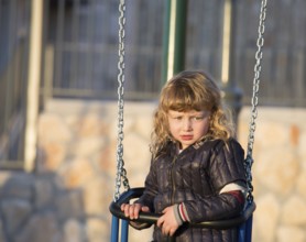 Adorable little boy in black jacket on a swing near the house