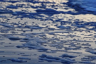 The sea waves and foam form textured patterns on the beach at dusk, Groede, Zeeland, Netherlands