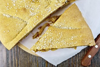 Pie with cabbage and sesame seeds with fresh rye dough knife on background wooden plank on top