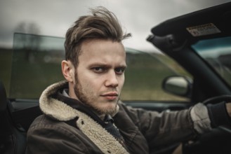 A serious-looking man driving a convertible in the countryside