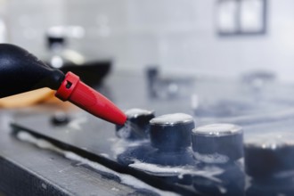 Close-up of a steam cleaner nozzle cleaning a stovetop