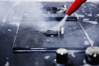 Focused image of water being sprayed from a red nozzle onto a stove