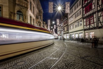 Langzeitbelichtung einer Straßenbahn, die durch eine historische Straße mit Fachwerkhäusern fährt,