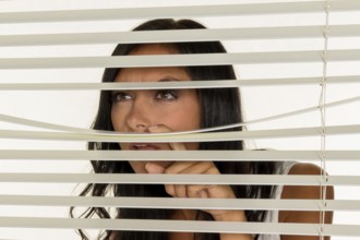 A young woman watches something through the blinds of her window Austria
