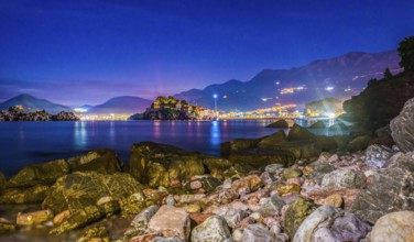 Stones on the coast of Adriatic sea near illuminated Sveti Stefan at sunset, Montenegro, Europe