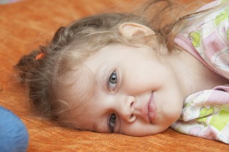 Cheerful three year old girl lying on the bed and looked into the frame