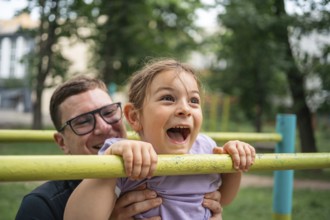 Father with child girl doing pull-ups on workout outdoor area. Healthy active lifestyle, happy