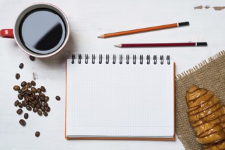 Opened notepad and cup of coffee with donut on wooden table