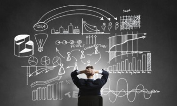 Rear view of businessman sitting in office chair and looking at infographs on chalkboard
